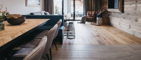 Un espacio de estar moderno con techo de madera, una zona de comedor con mesa y sillas de madera, un sofá y un televisor montado en la pared.