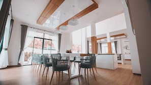 A modern dining area with a wooden ceiling, large windows, and a view of trees. - Happy Family Villa (Chalong)