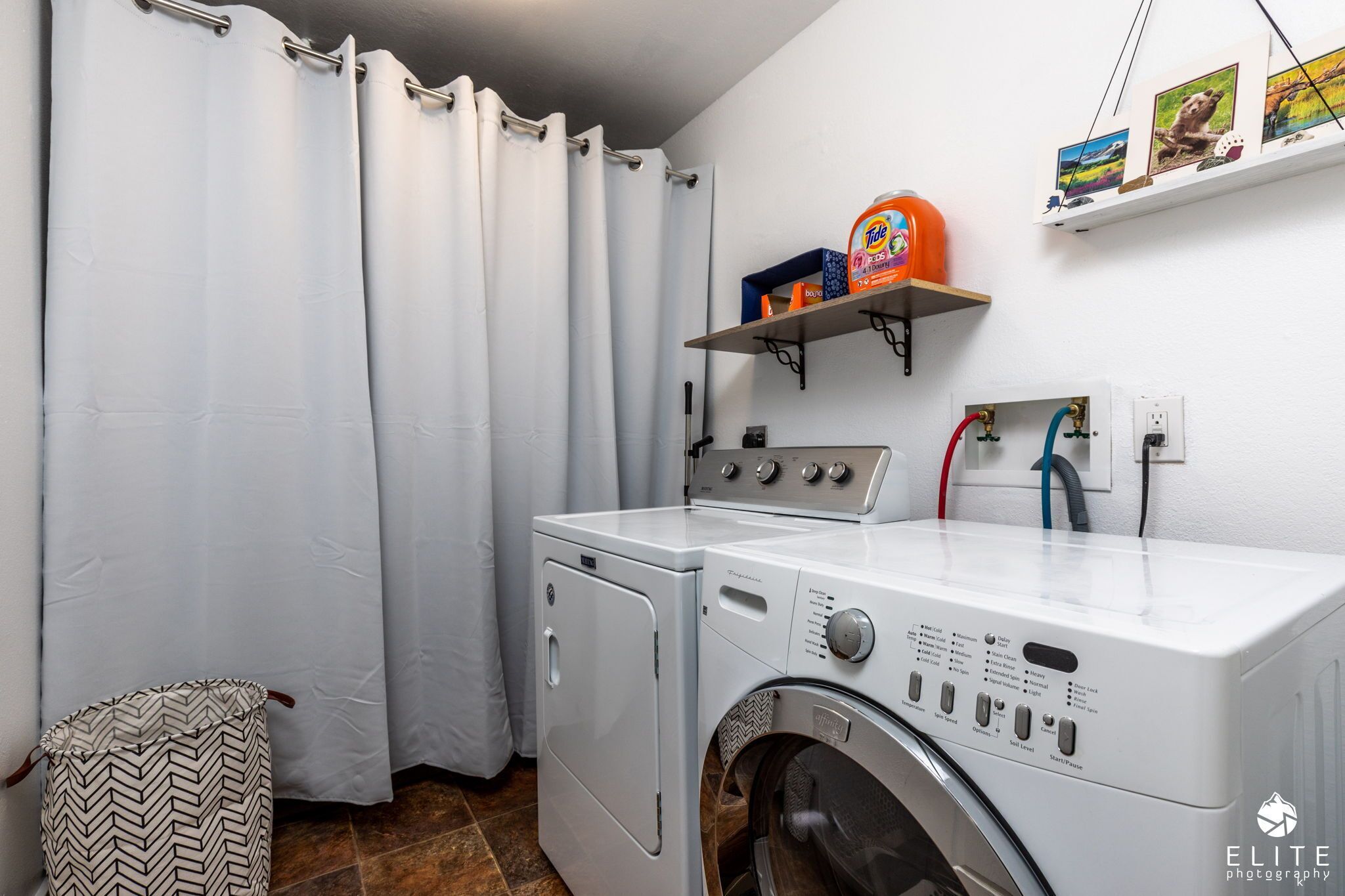 Un cuarto de lavado con lavadora y secadora de carga frontal, un estante con detergente para la ropa y un enchufe.