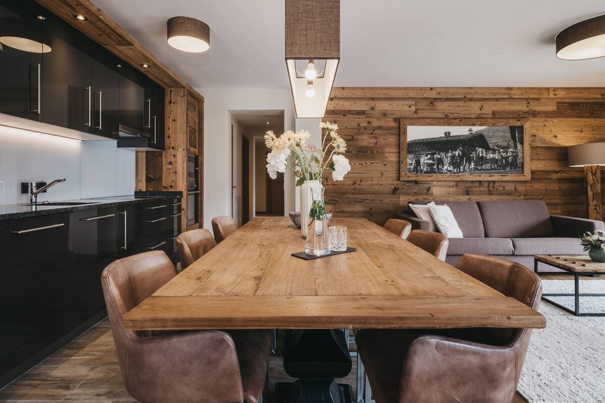 A modern kitchen with dark cabinets, a wooden dining table, and leather chairs.