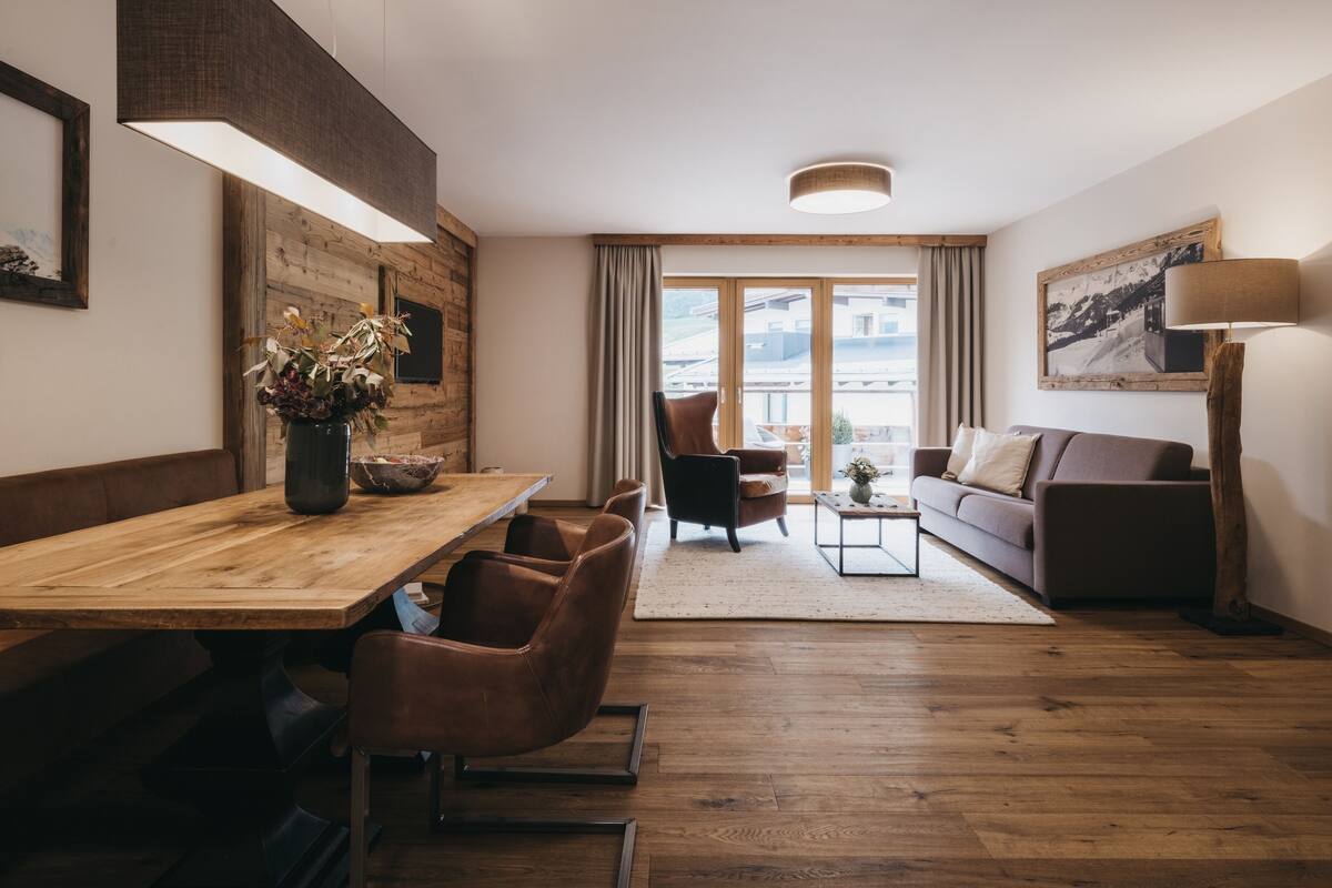 A modern living room with a wooden dining table, leather chairs, a sofa, and a floor lamp.