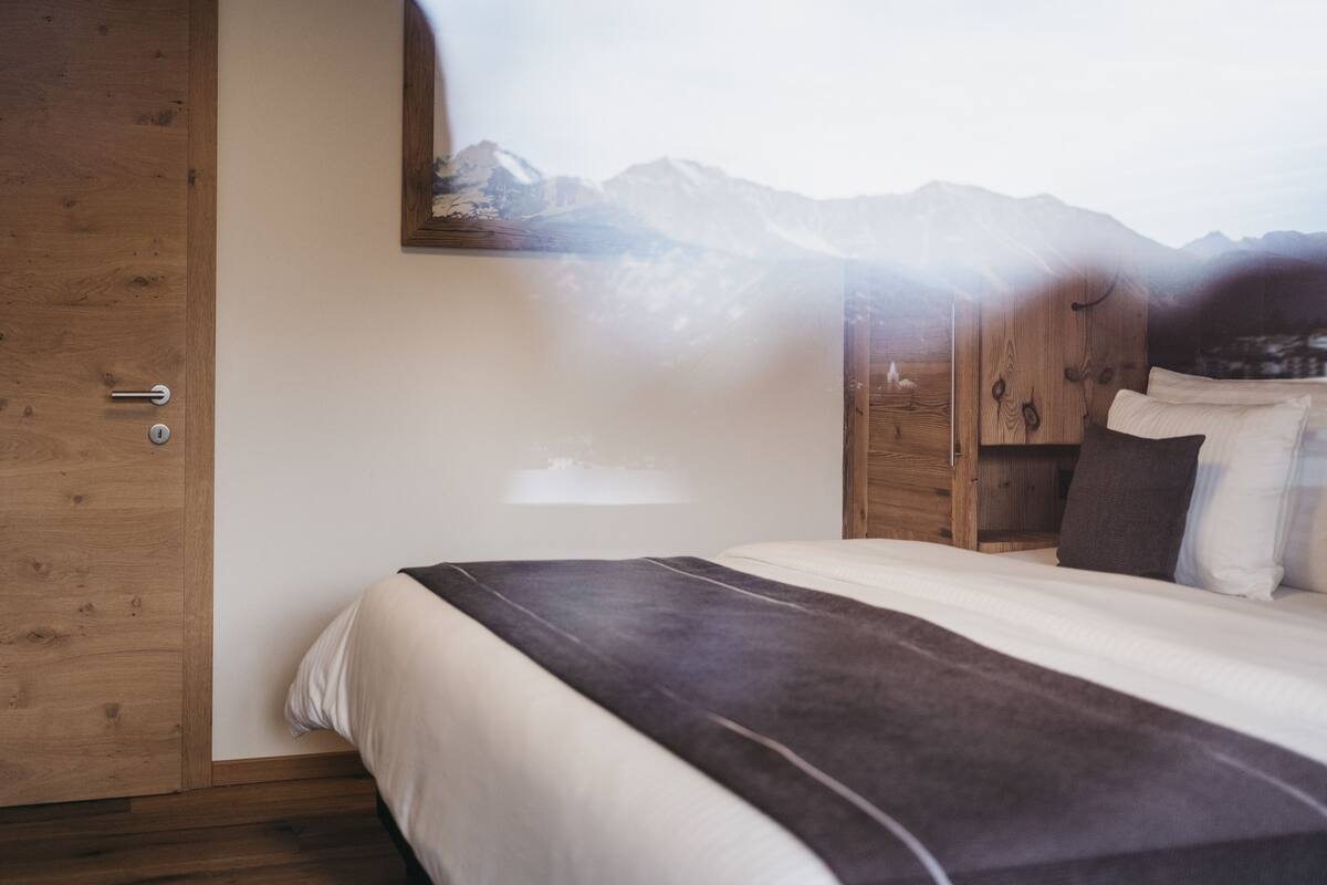 A bedroom with a bed, wooden wardrobe, and a mountain view.