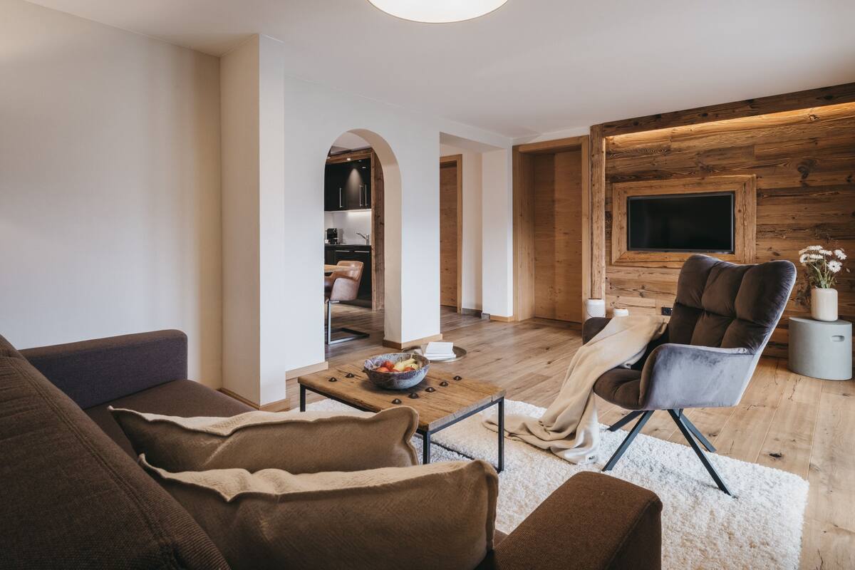 A modern living room with a sofa, armchairs, a coffee table, and a TV mounted on a wooden wall.