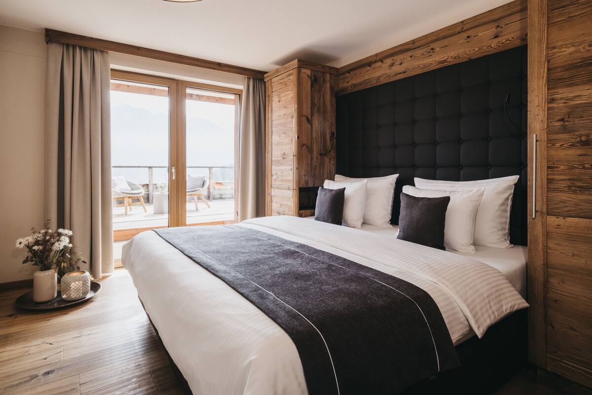 A modern bedroom with a large bed, wooden headboard, and a balcony view.