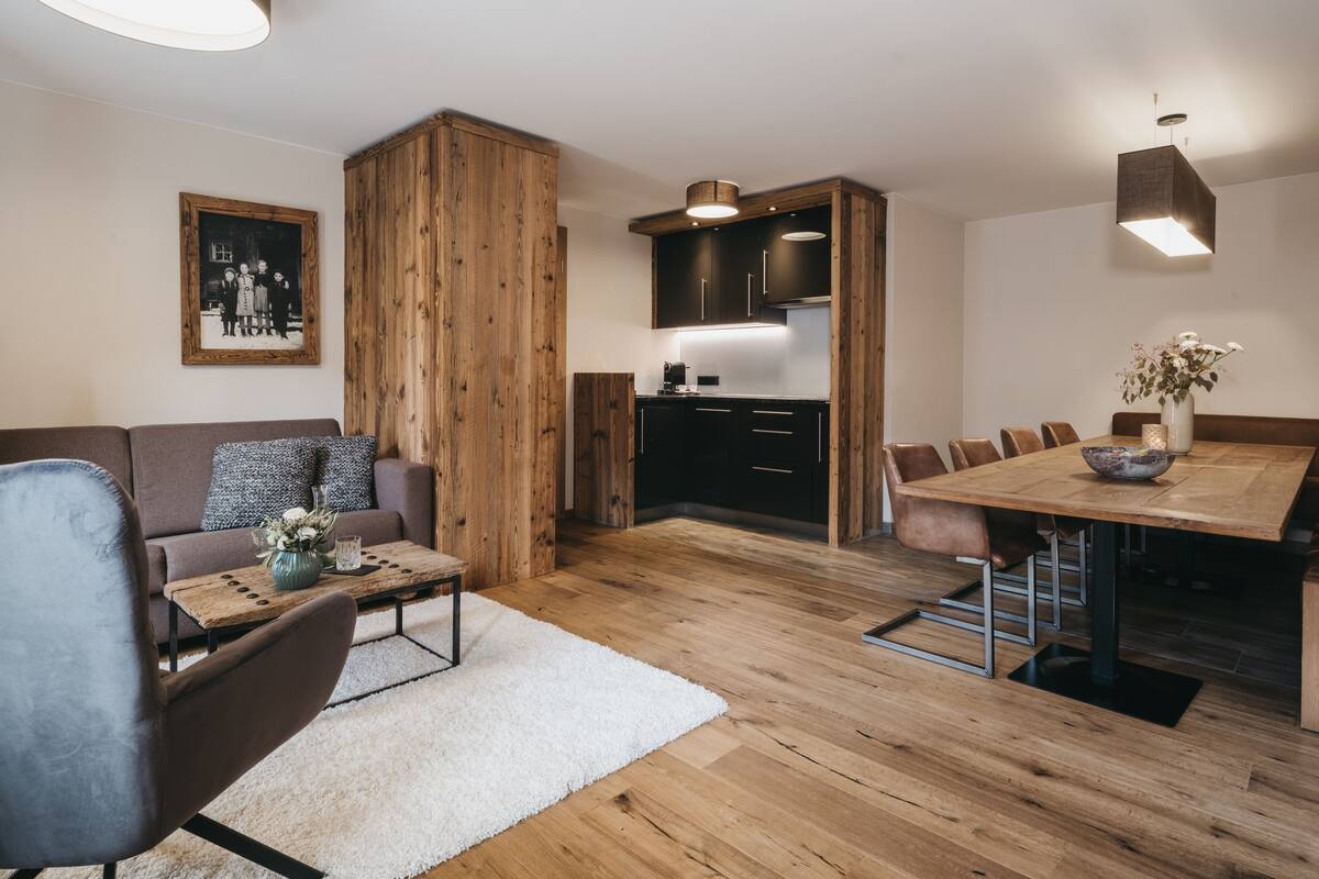 A modern living room with a wooden floor, a sofa, a coffee table, and a dining area with a wooden table and chairs.