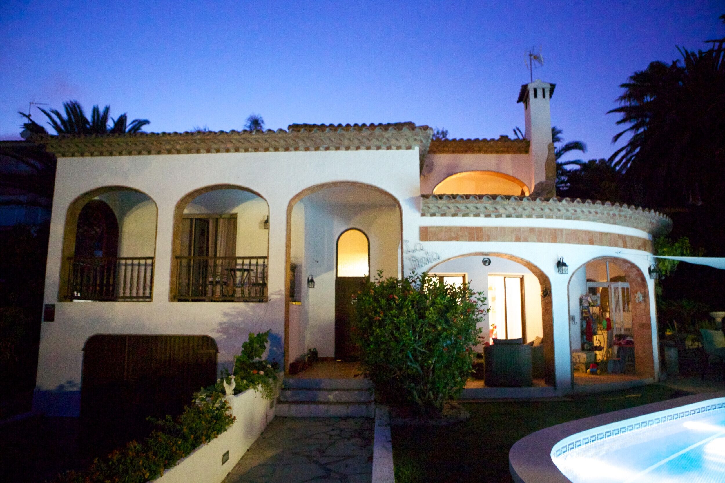 A two-story house with a swimming pool, arched windows, and a small tower.