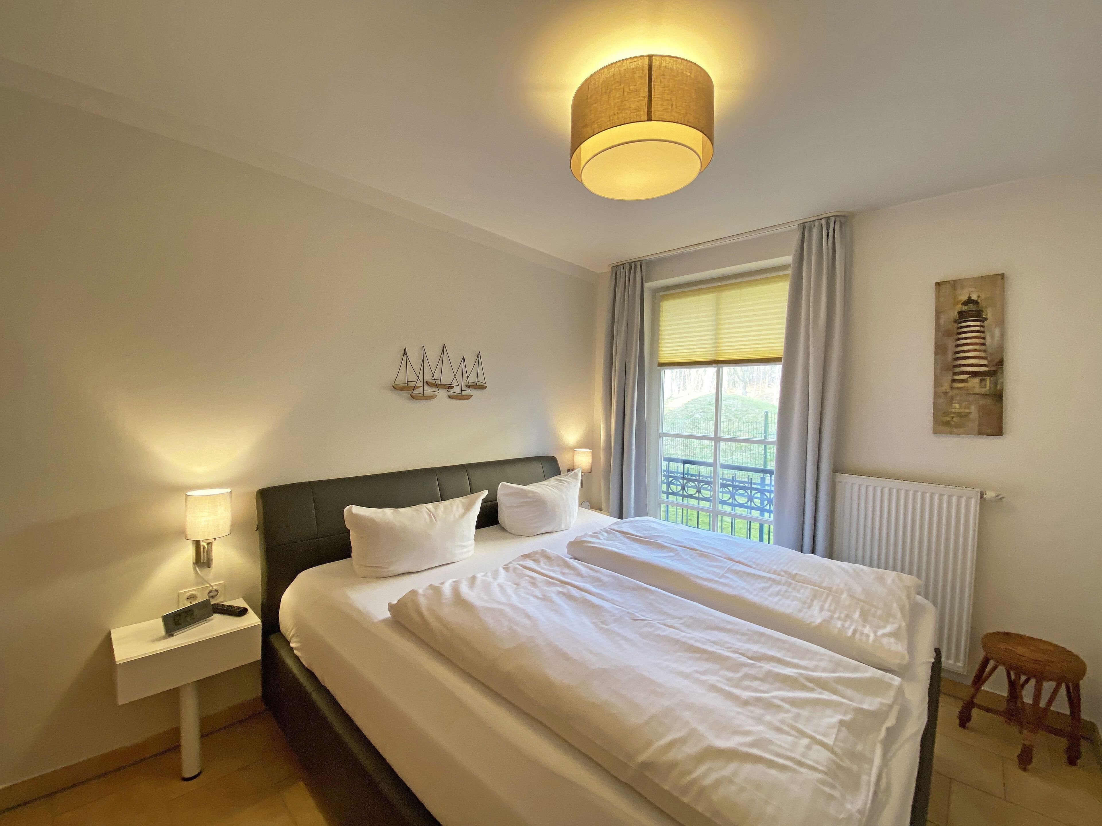 A hotel room with a large bed, a bedside table with a lamp, a window with curtains, and a wall-mounted artwork.