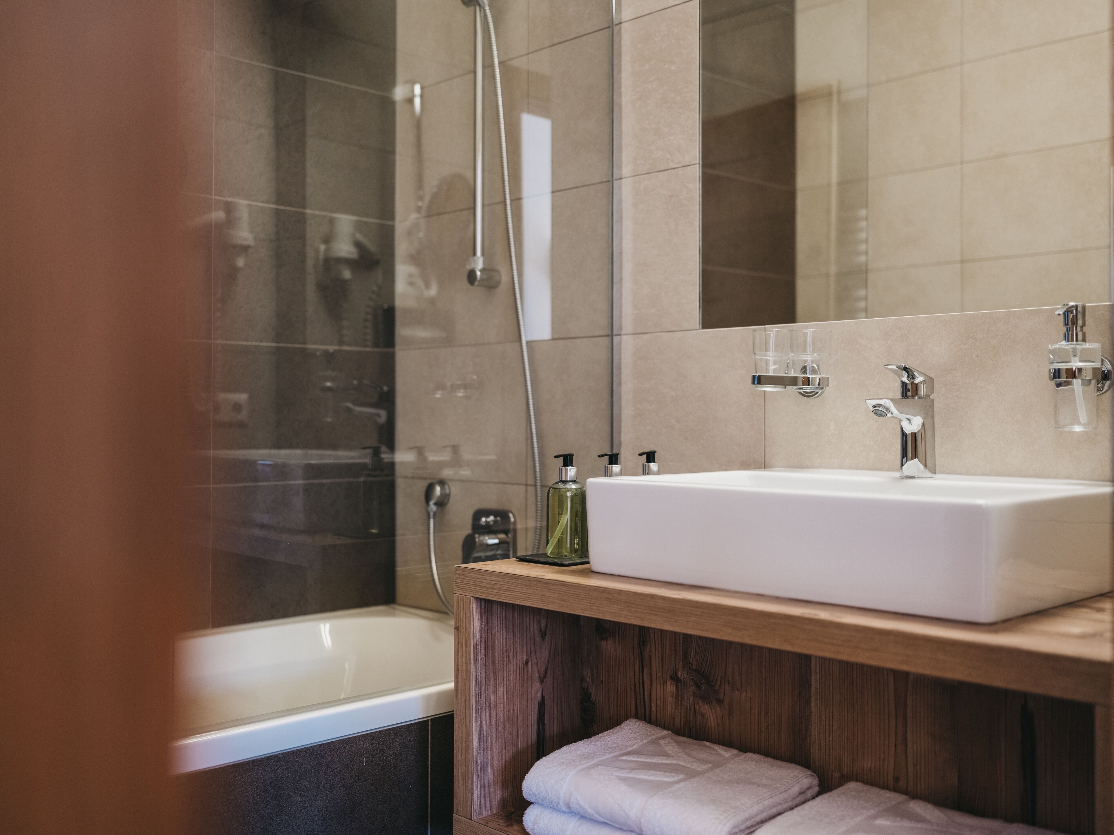 Un baño moderno con un lavamanos blanco, cabina de ducha de vidrio y tocador de madera.