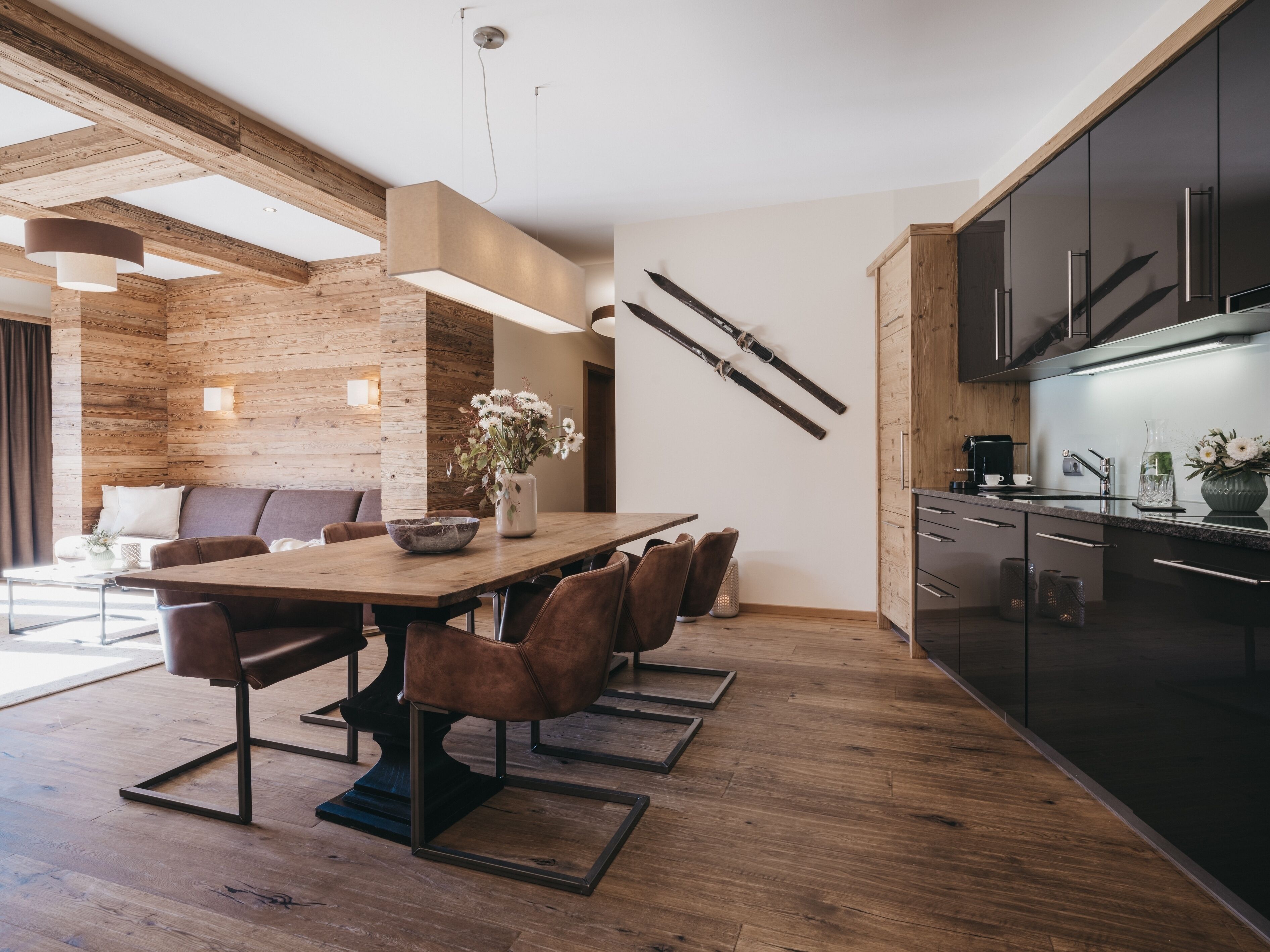 A modern kitchen with dark cabinets, a wooden dining table, and a hanging ski rack.