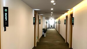 Pasillo de hotel con puertas numeradas, una planta en maceta y una alfombra con diseños circulares.