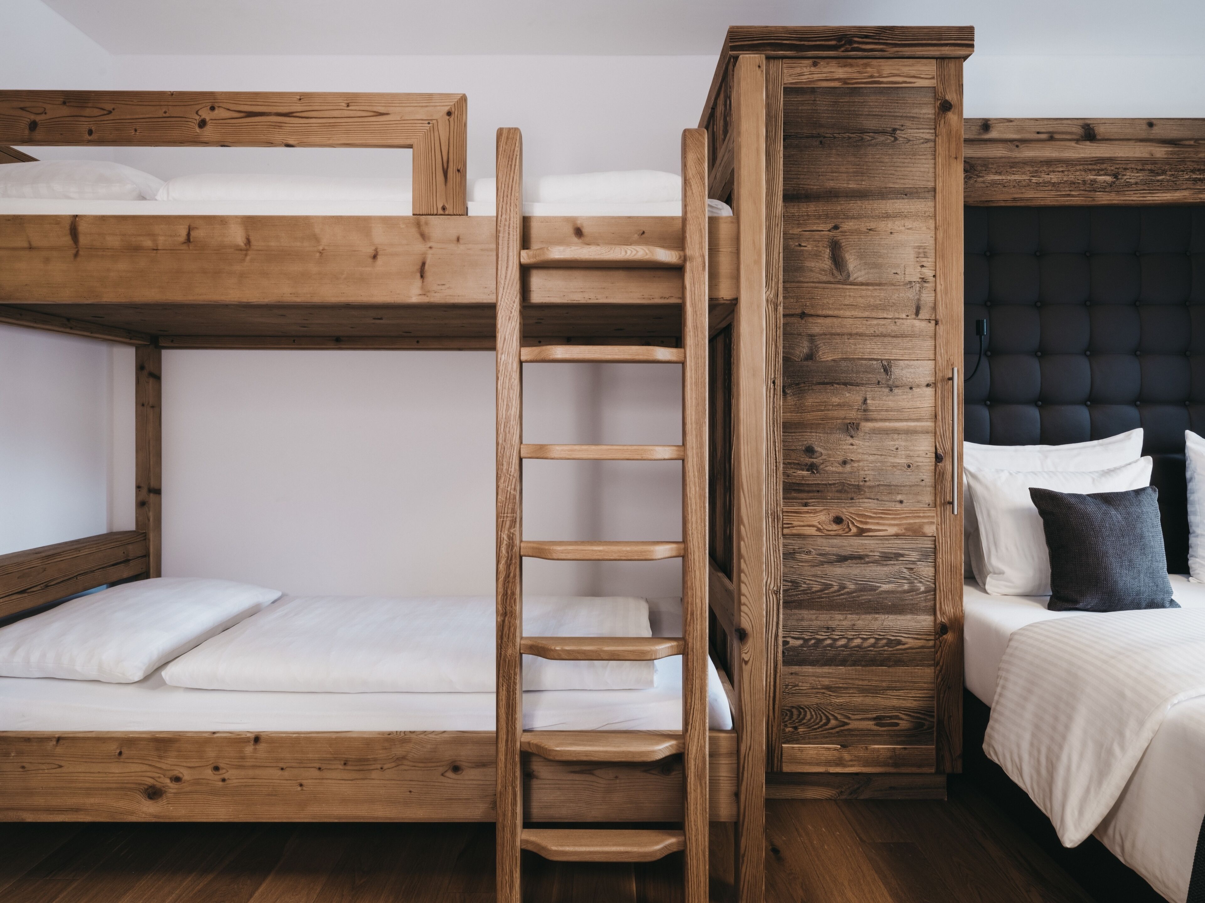 A bunk bed with a wooden ladder, a separate bed with a dark headboard, and a wooden wardrobe.