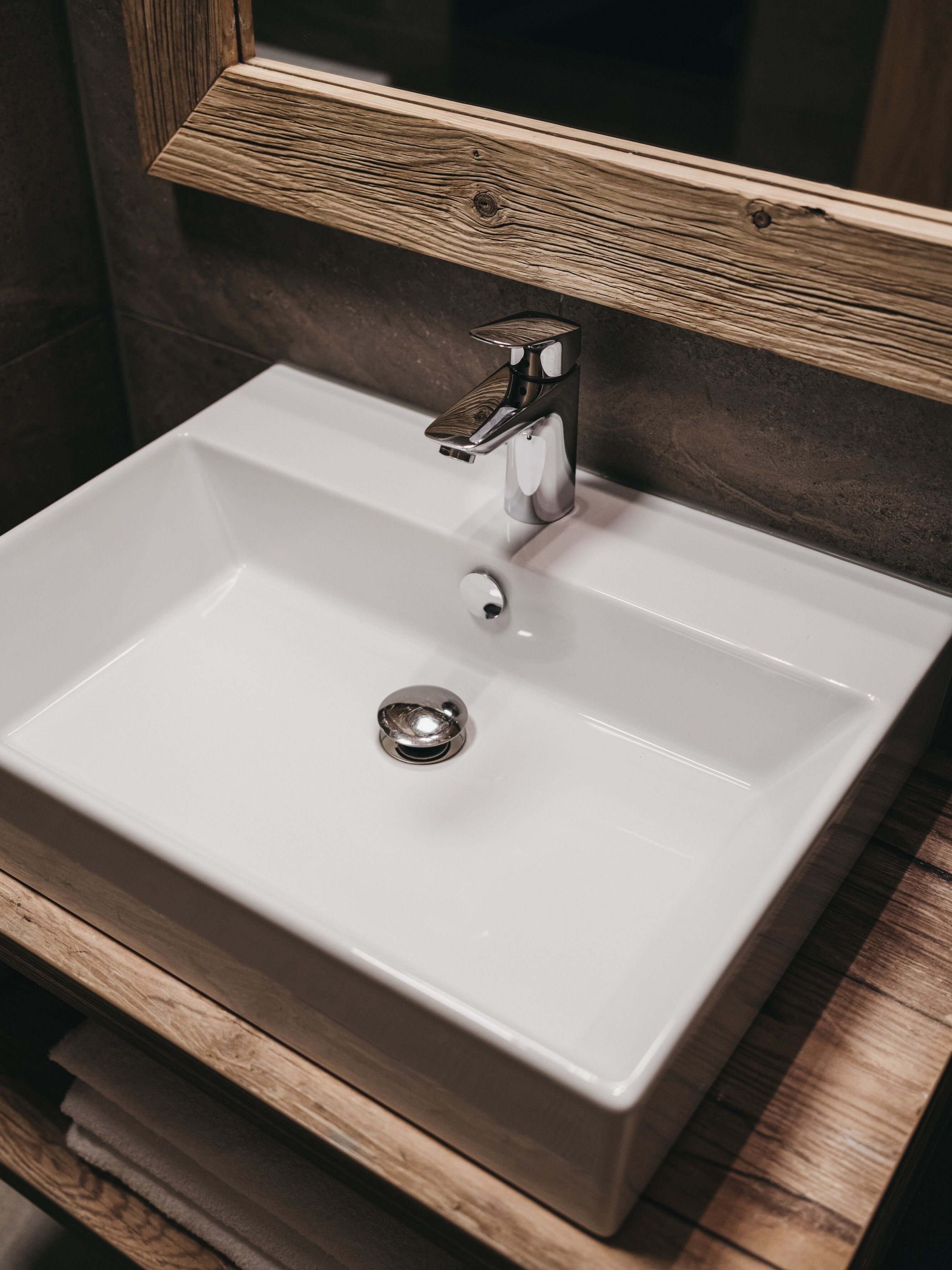 A bathroom with a white sink, a wooden vanity, and a mirror above the sink.
