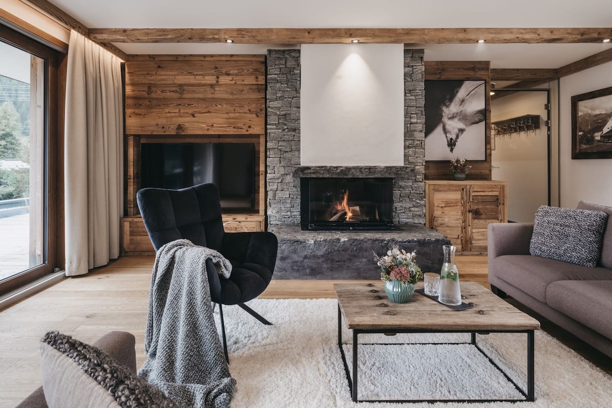 A modern living room with a stone fireplace, wooden beams, a comfortable sofa, and a large window.
