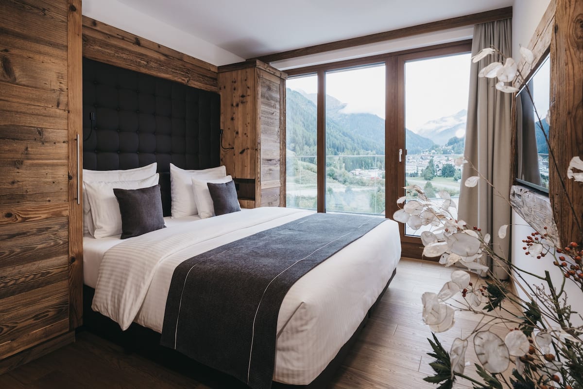 A bedroom with a large bed, wooden walls, and a view of mountains through a large window.