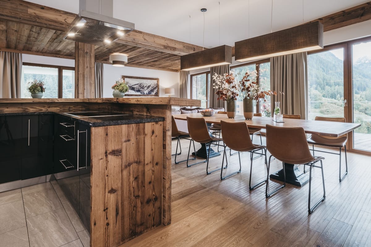 A modern kitchen with a wooden island, a dining area with a large table and chairs, and a view of mountains through large windows.