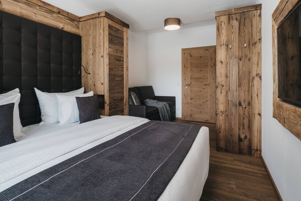 A bedroom with a large bed, wooden wardrobe, and a small seating area.