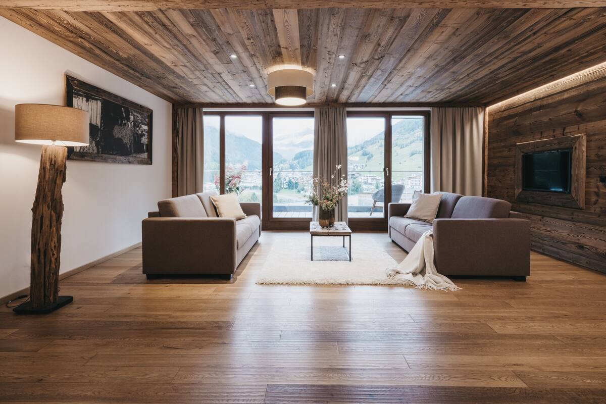 A spacious living room with wooden flooring, two sofas, a coffee table, and a large window offering a mountain view.