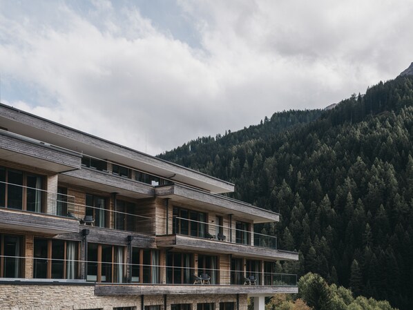 A modern multi-story building with a stone facade, large windows, and a balcony area. - VAYA St. Anton (Sankt Anton am Arlberg)