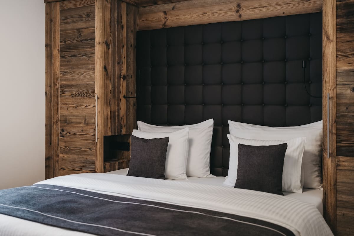 A bedroom with a wooden headboard, a tufted upholstered headboard, and a bed with white and dark pillows.