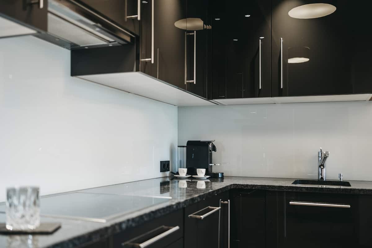 A modern kitchen with black cabinets, a black countertop, a coffee maker, and a sink.