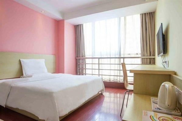 Een hotelkamer met een bed, een bureau, een stoel, een televisie en een raam met gordijnen.