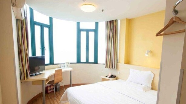 A hotel room with a bed, a desk with a computer, a chair, and a window with curtains.