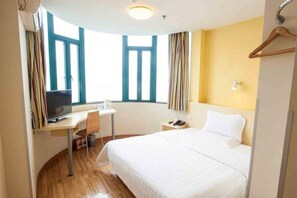 Hotellihuone, jossa on sänky, työpöytä tietokoneella, tuoli ja ikkuna, jossa on verhot.