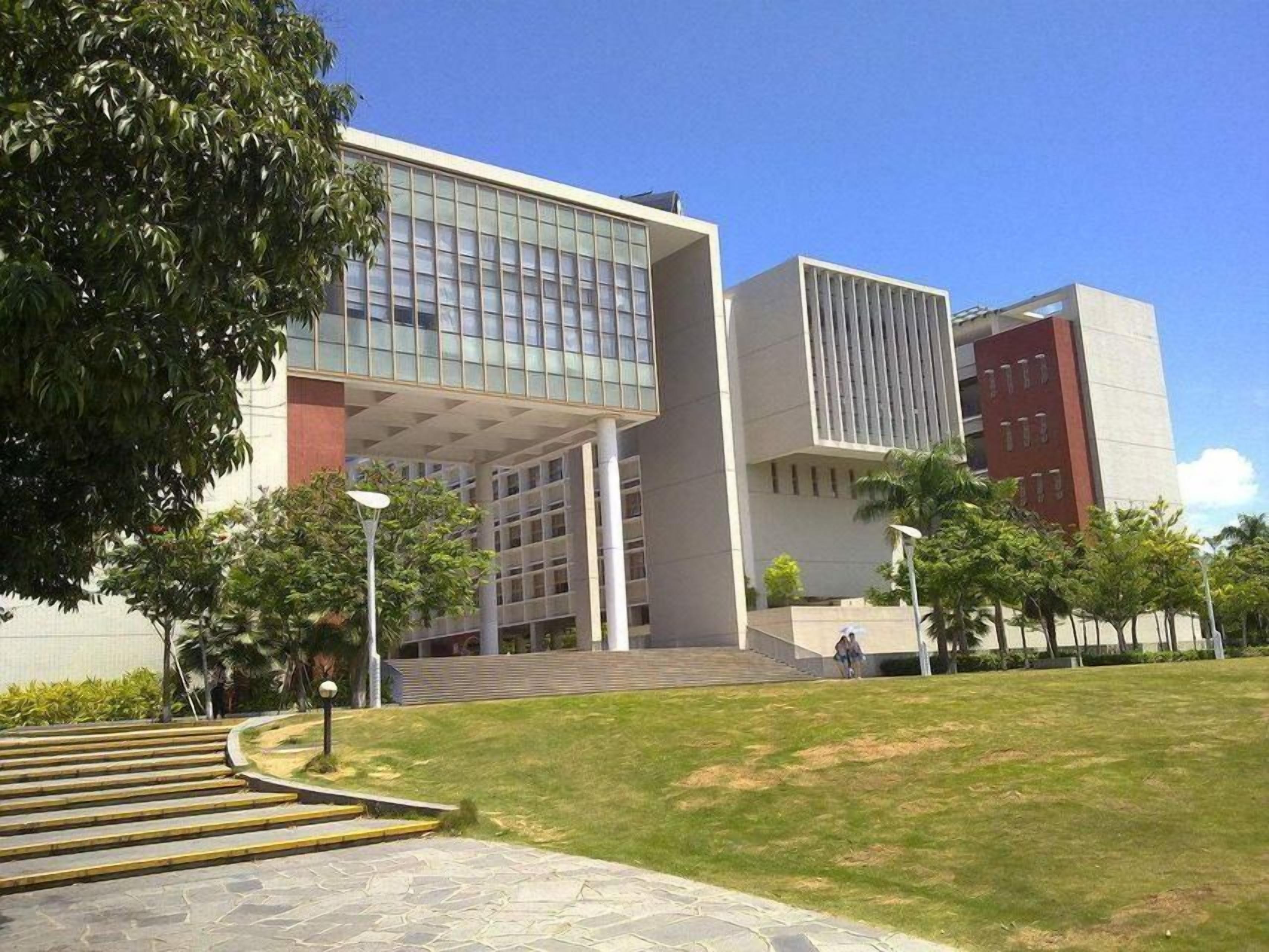 A modern building with a glass facade, a flat roof, and a paved entrance area with steps.