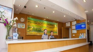 A reception desk with a wooden finish, a large landscape painting above it, and a digital display on the wall.