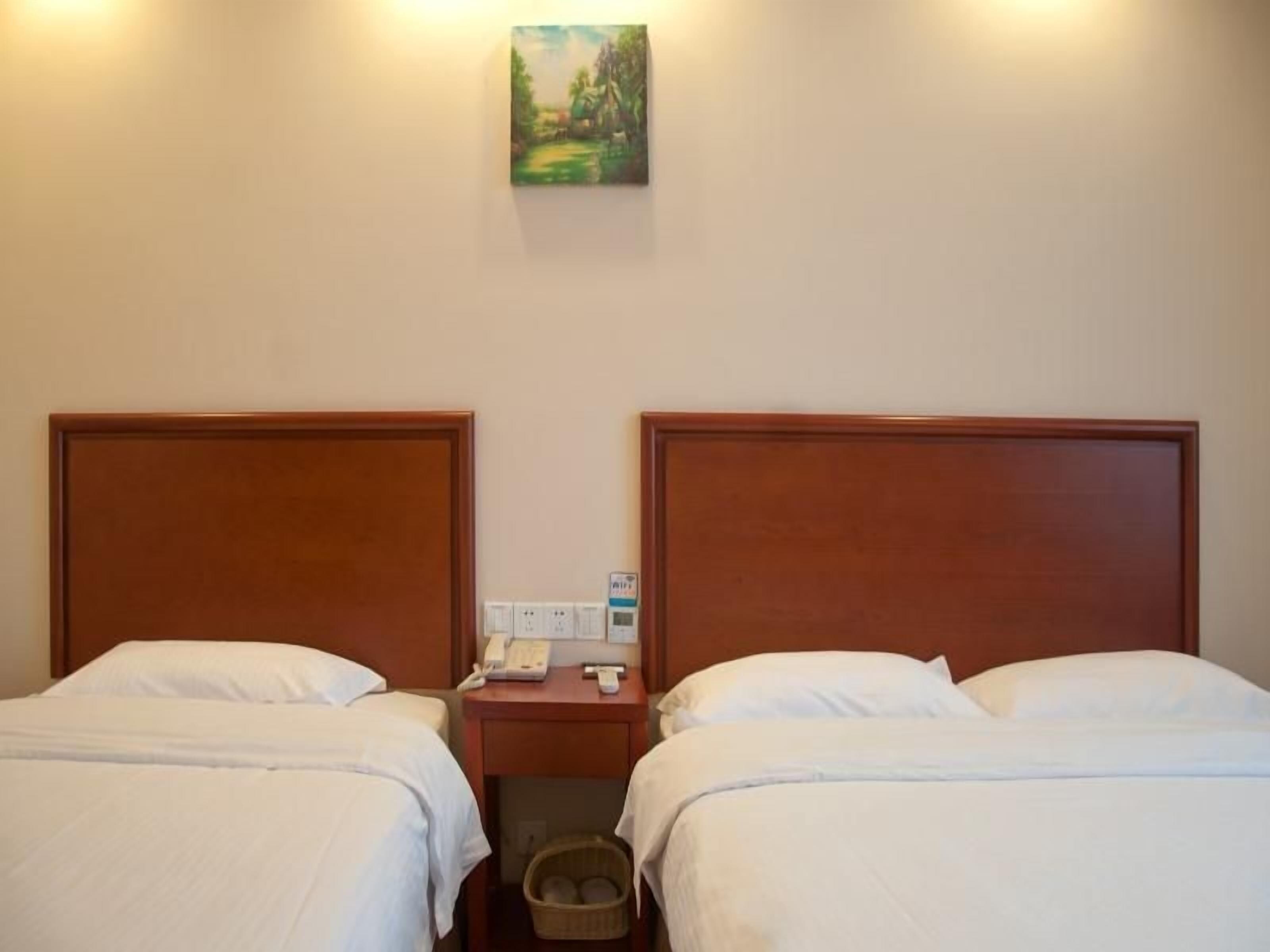 A hotel room with two single beds, a nightstand with a phone and a lamp, and a painting on the wall.