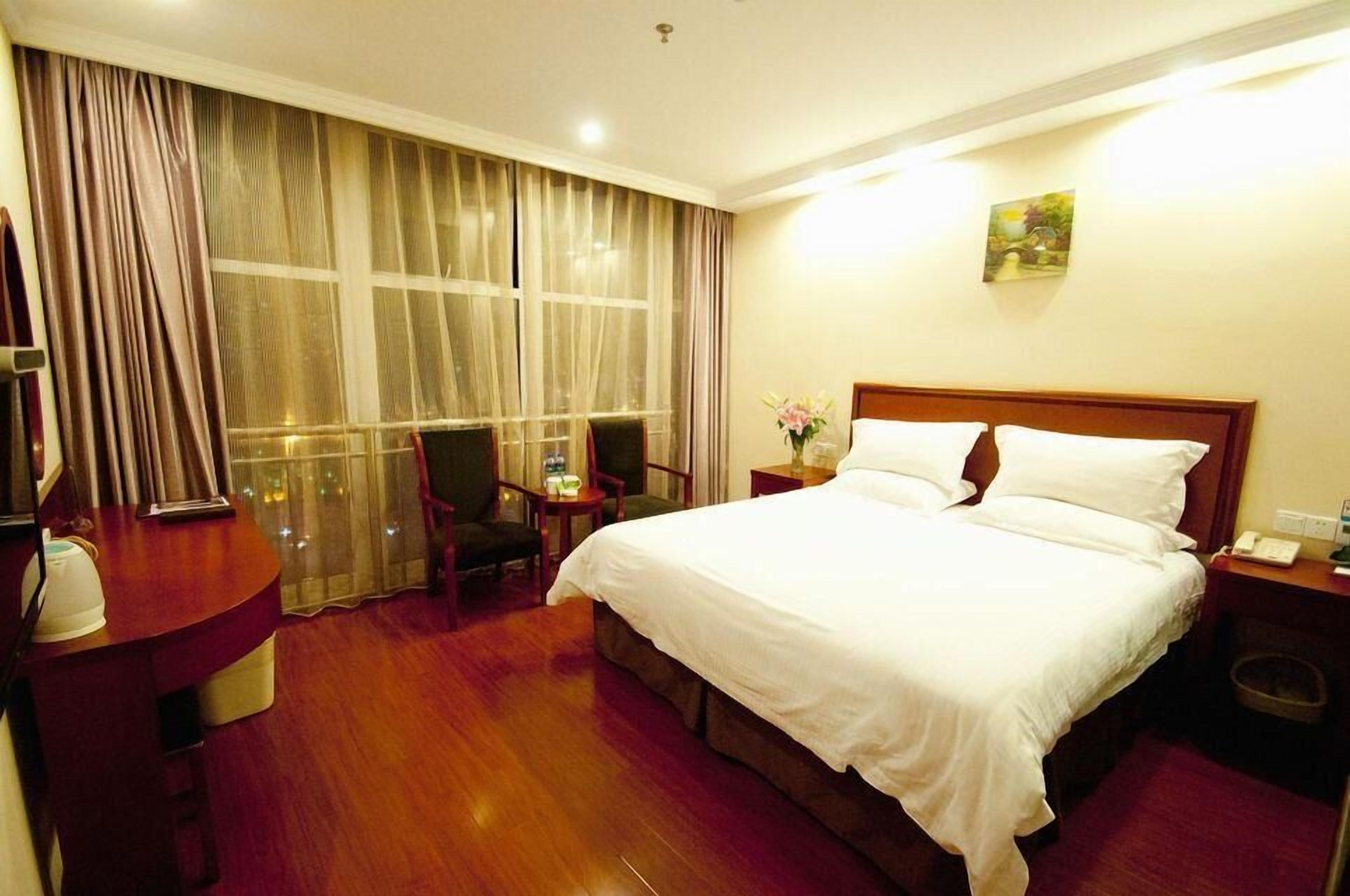 A hotel room with a large bed, a desk, a chair, a nightstand, and a window with curtains.