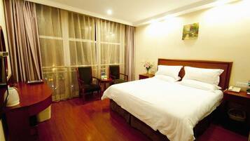 A hotel room with a large bed, a desk, a chair, a nightstand, and a window with curtains.