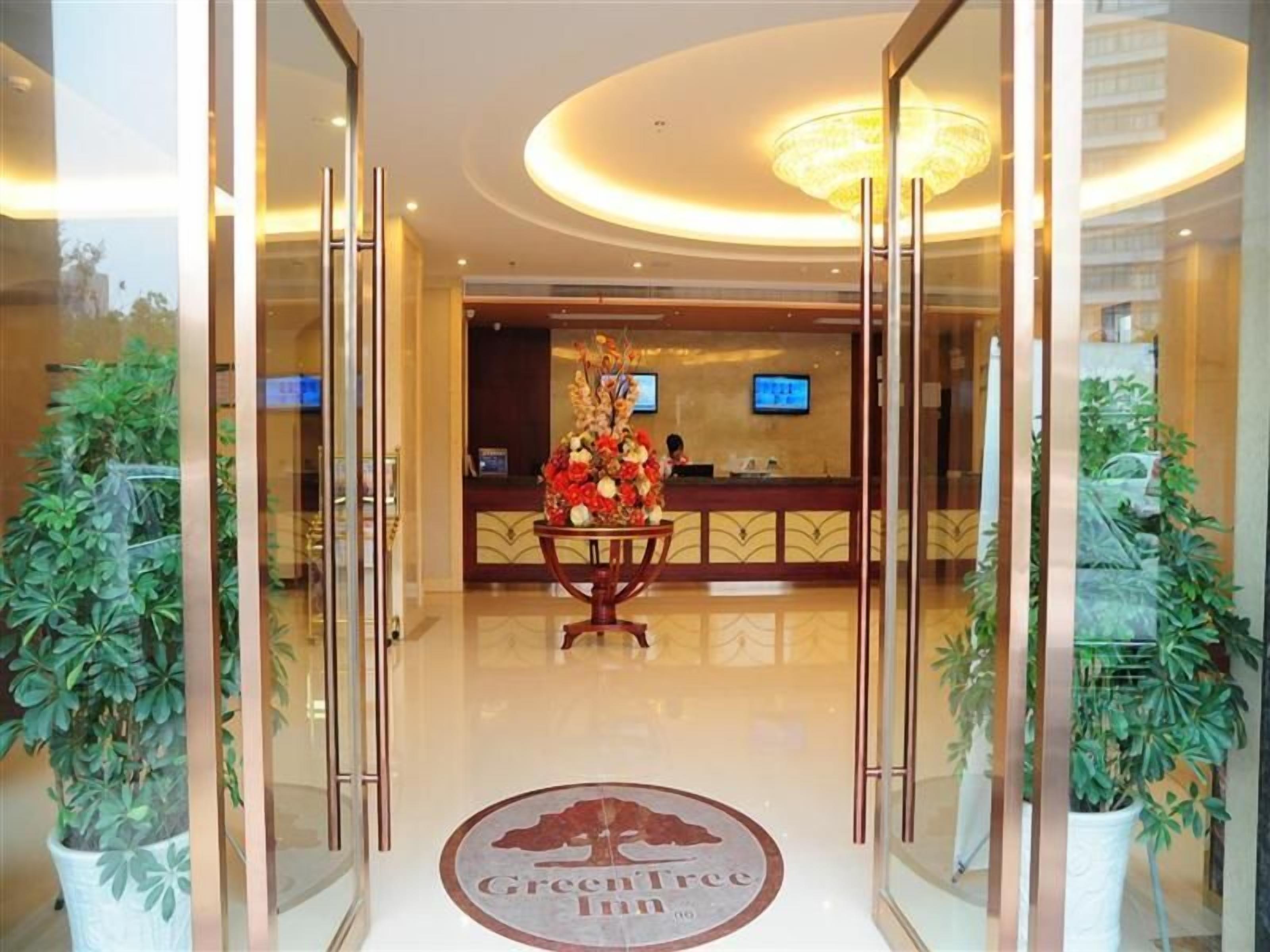 Vestíbulo de hotel con mostrador de recepción, candelabro y plantas en macetas.