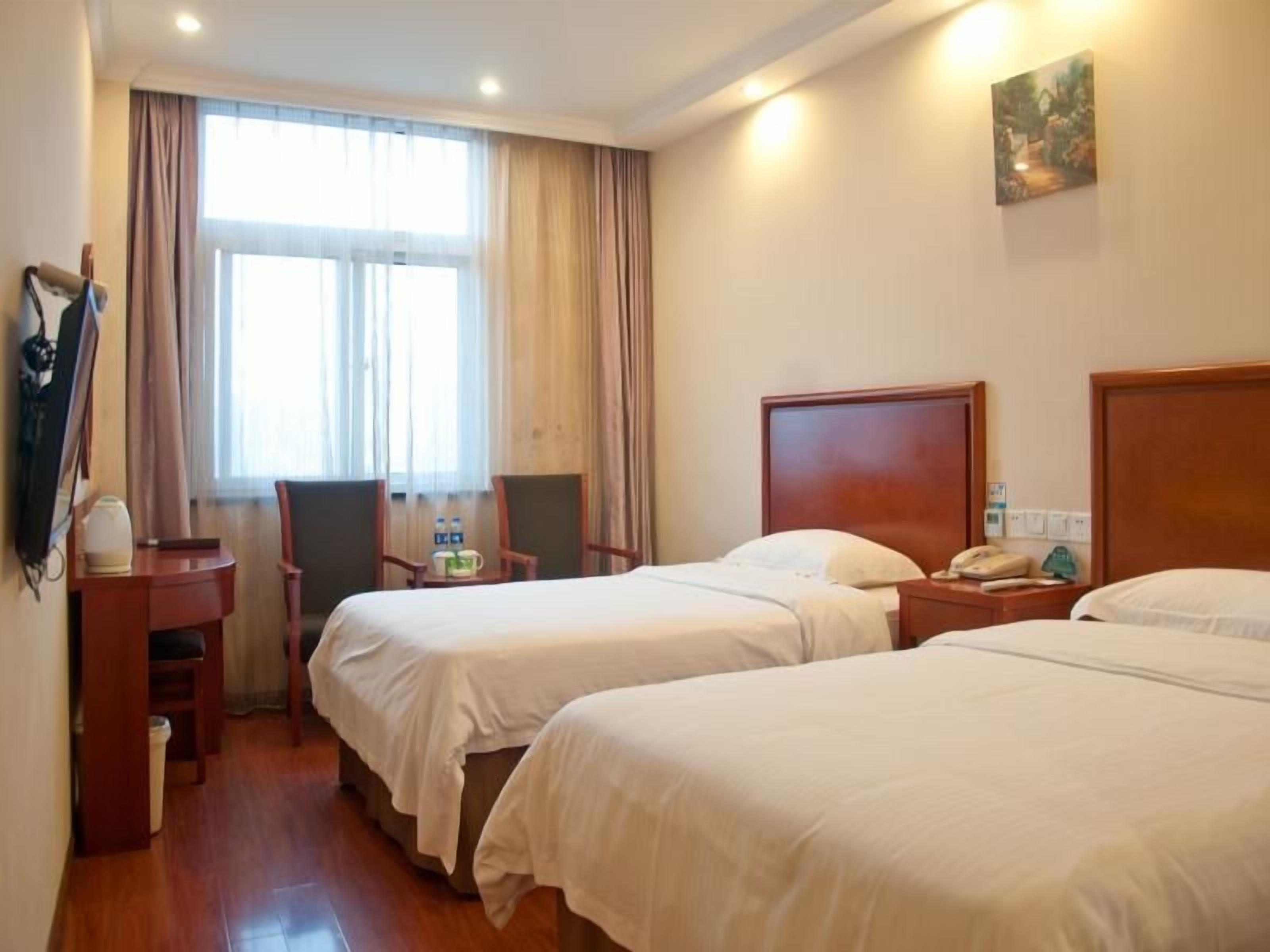 A hotel room with two beds, a desk, a chair, a window with curtains, and a painting on the wall.