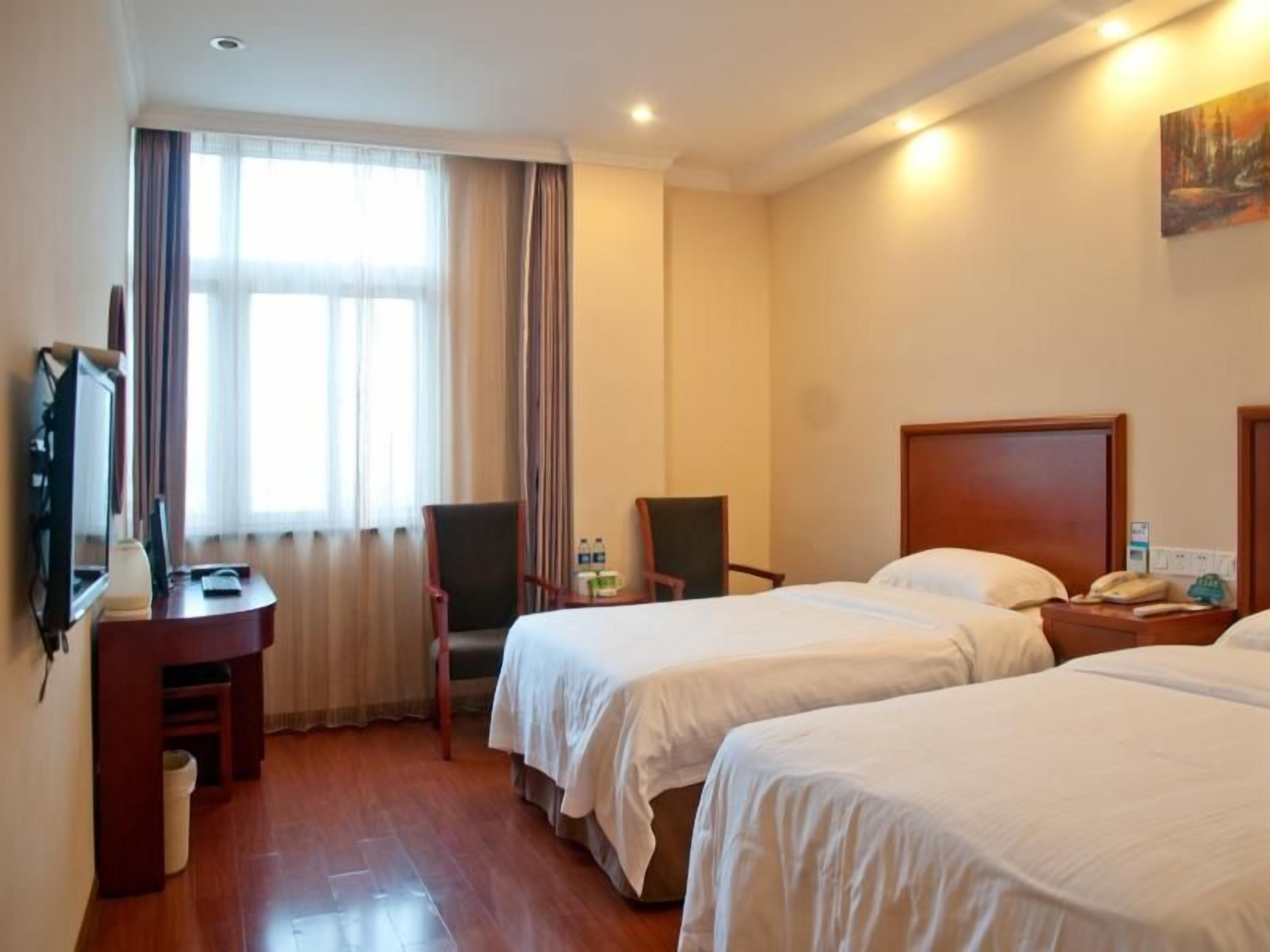 Quarto de hotel com duas camas, uma escrivaninha, uma cadeira e uma televisão.