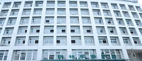 A multi-story hotel building with a green and white facade, featuring a prominent sign at the top.