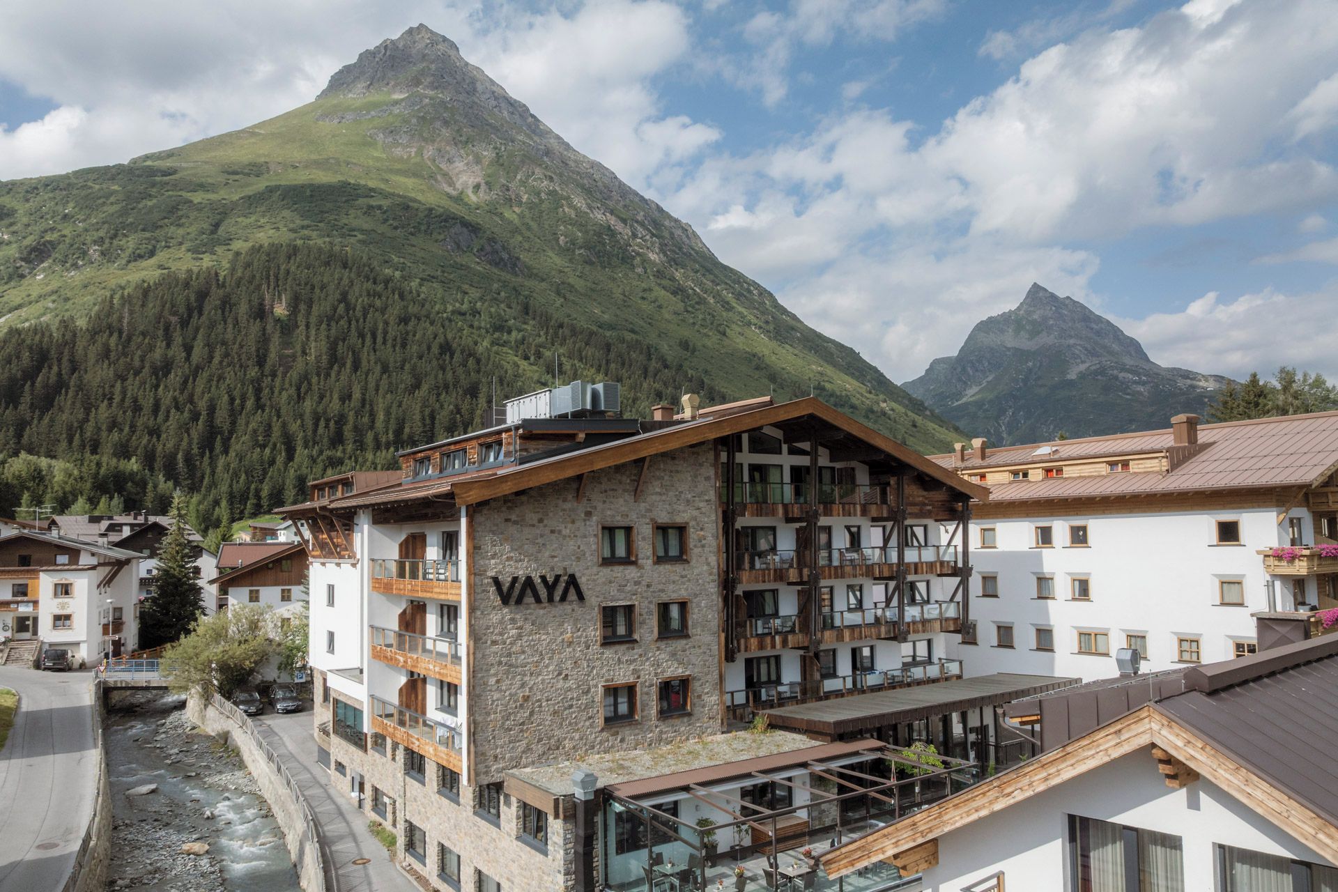 Un chalet de montagne à la façade en pierre, doté de nombreux balcons et offrant une vue sur une chaîne de montagnes.
