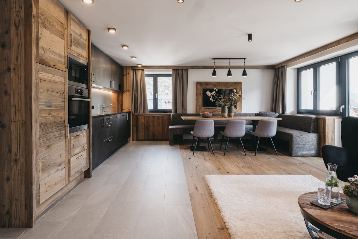 A modern kitchen with wooden cabinetry, a dining area with a bench, and a large window providing natural light.