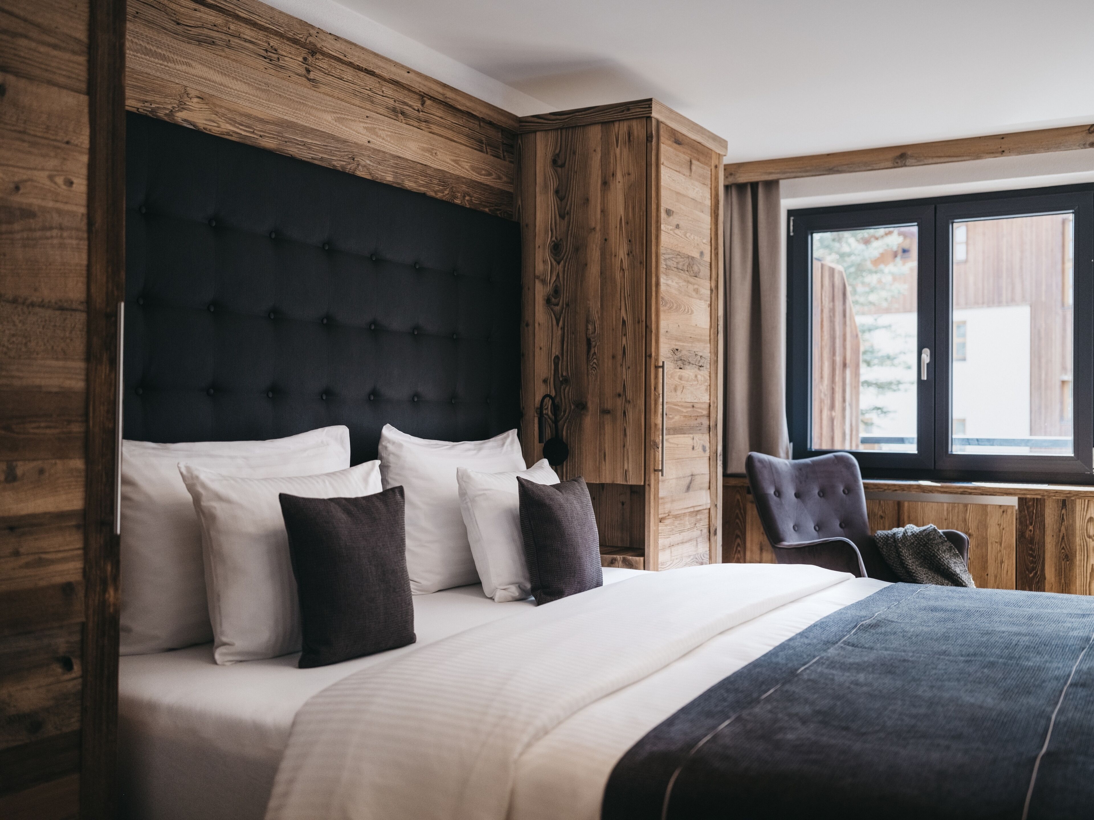 A bedroom with a large bed, wooden paneling, and a window with a view.