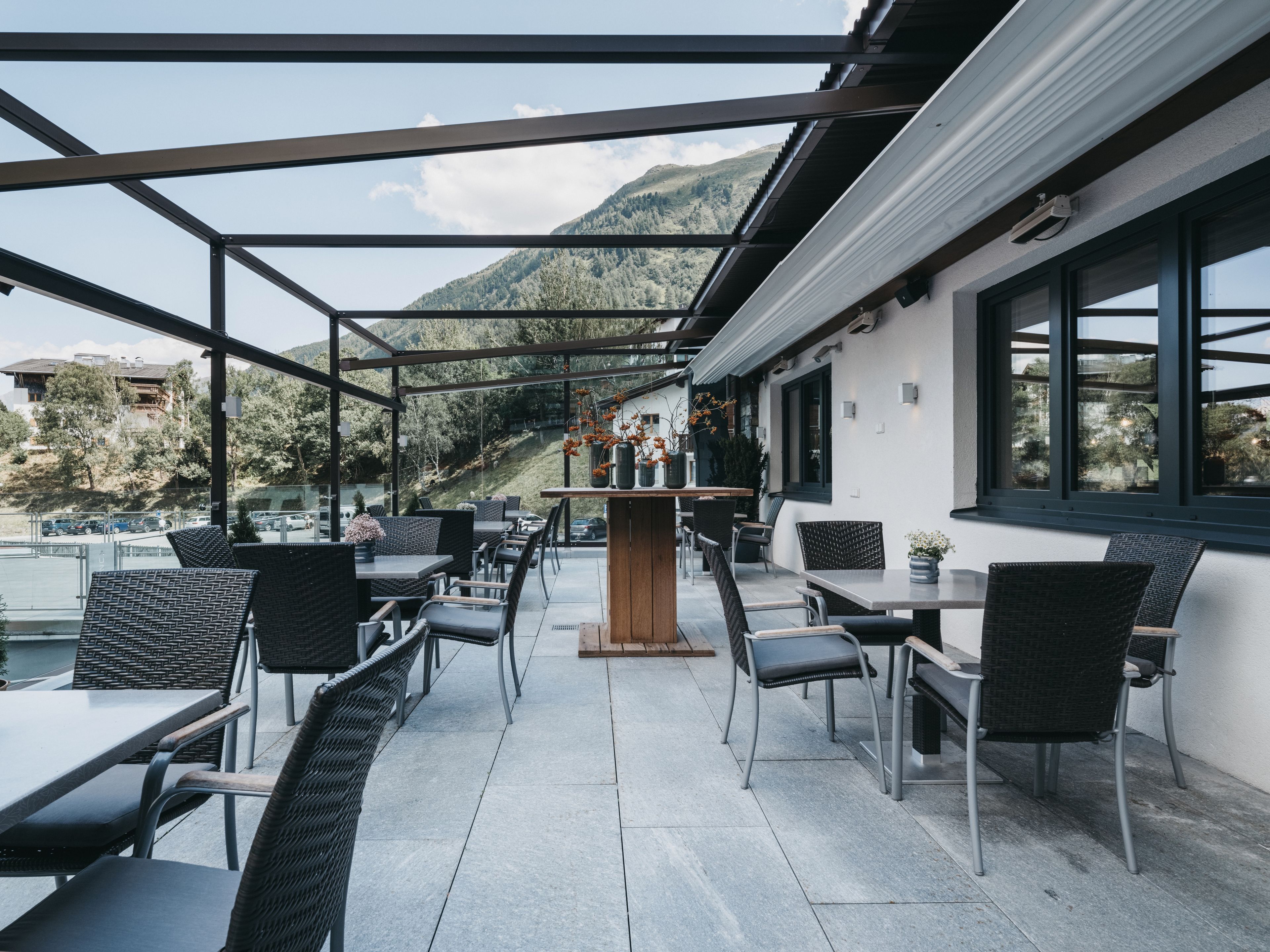 An outdoor seating area with tables and chairs, a central bar, and a view of a mountainous landscape.