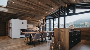 A modern kitchen with a wooden ceiling, large windows, and a dining area with grey chairs. - VAYA Galtür Paznaun (Galtur)
