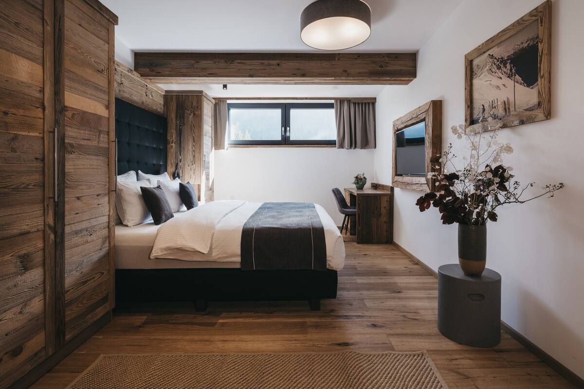 A modern bedroom with a large bed, wooden walls, a desk, and a window.