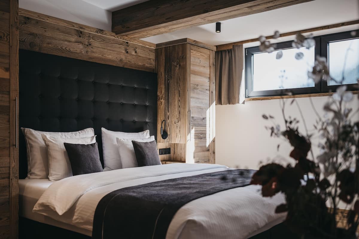 A bedroom with a dark headboard, white bedding, and wooden paneling.