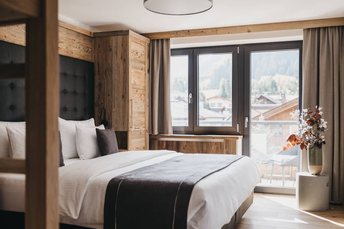A modern bedroom with a large bed, wooden headboard, and a view of a balcony.