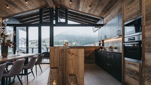 A modern kitchen with wooden accents, large windows, and a view of the mountains. - VAYA Galtür Paznaun (Galtur)