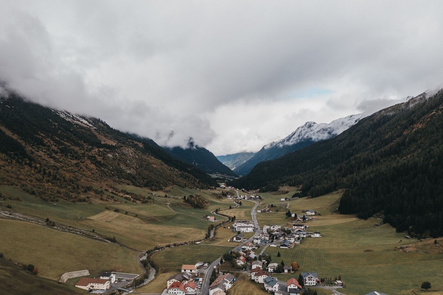A valley with a small town, surrounded by mountains and covered in clouds.