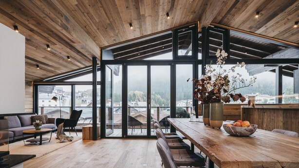 A modern kitchen with a wooden ceiling, large windows, and a dining area with a wooden table and chairs. - VAYA Galtür Paznaun (Galtur)