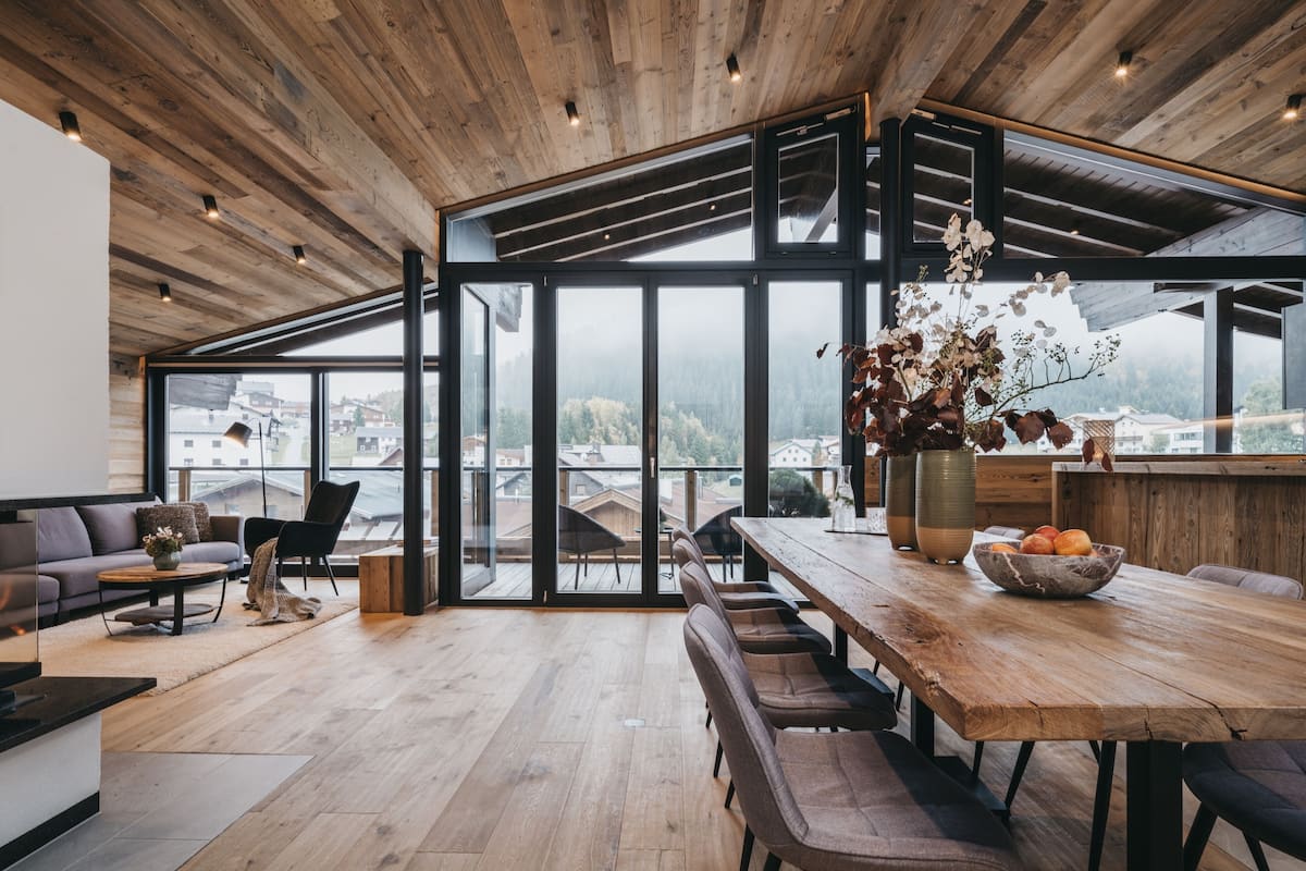 A modern kitchen with a wooden ceiling, large windows, and a dining area with a wooden table and chairs.