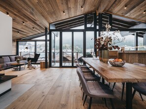 A modern kitchen with a wooden ceiling, large windows, and a dining area with a wooden table and chairs. - VAYA Galtür Paznaun (Galtur)