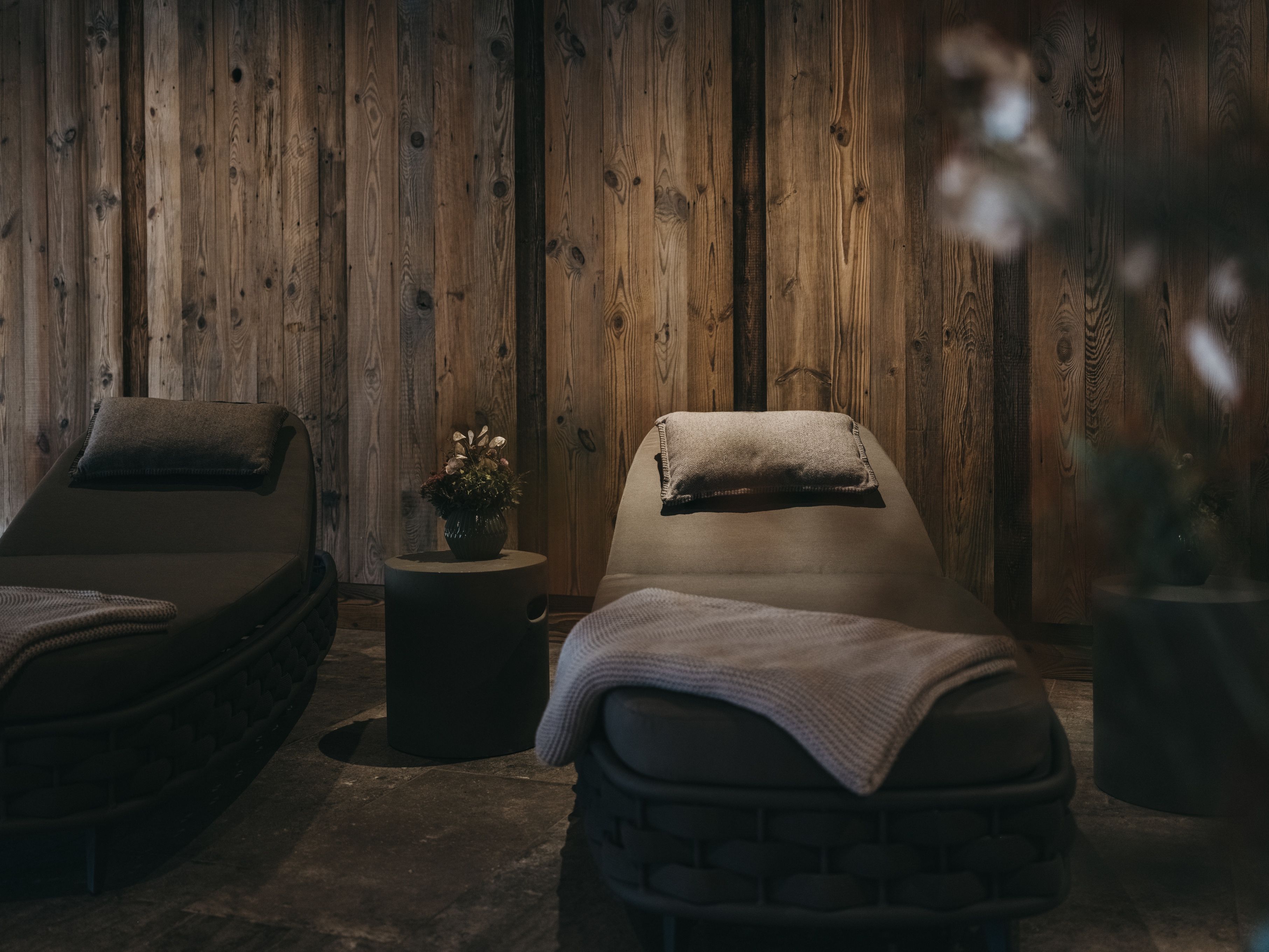 A spa room with two massage beds, a small round table with a plant, and wooden paneling on the walls.